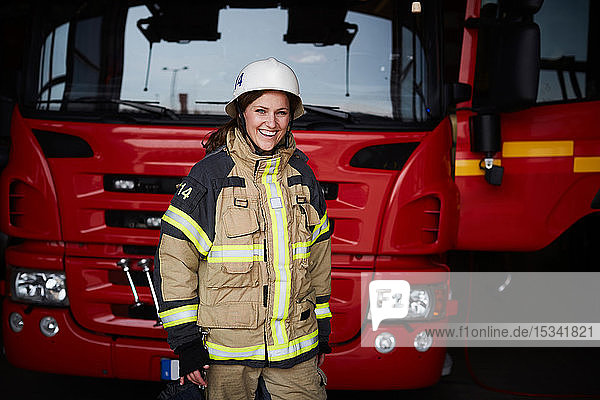 Porträt einer lächelnden Feuerwehrfrau  die vor dem Feuerwehrauto in der Feuerwache steht