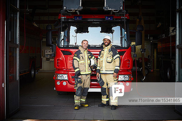 Portrait of firefighters standing in front of fire engine at fire station