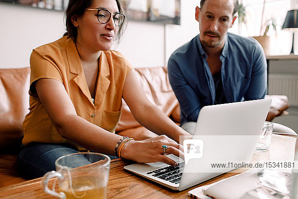 Geschäftsfrau tippt am Laptop  während sie mit einem männlichen Kollegen im Büro diskutiert