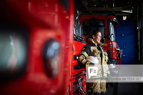 Smiling female firefighter standing by fire engine at fire station