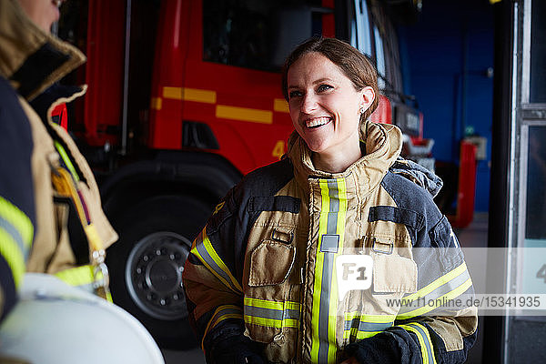 Smiling female firefighter looking at coworker while communicating in fire station