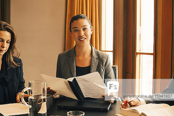Porträt einer lächelnden Rechtsanwältin mit Dokument am Konferenztisch im Büro