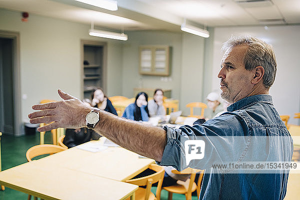 Senior male teacher gesturing while teaching during lesson in classroom