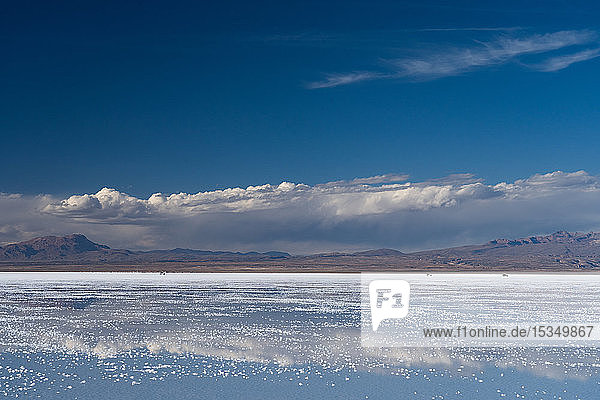 Die Schönheit der Salzebenen  in denen sich die Wolken und Berge nach Regenfällen spiegeln  drei 4WD-Fahrzeuge in der Ferne  Uyuni  Bolivien  Südamerika