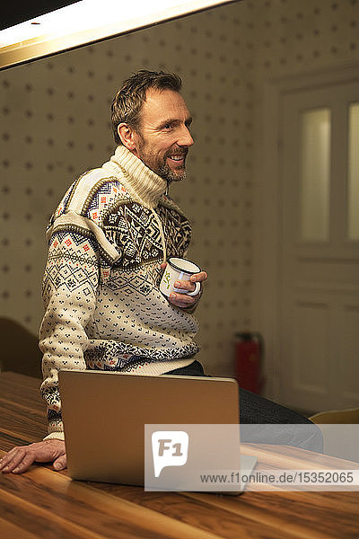 Smiling casual businessman with laptop on table at home