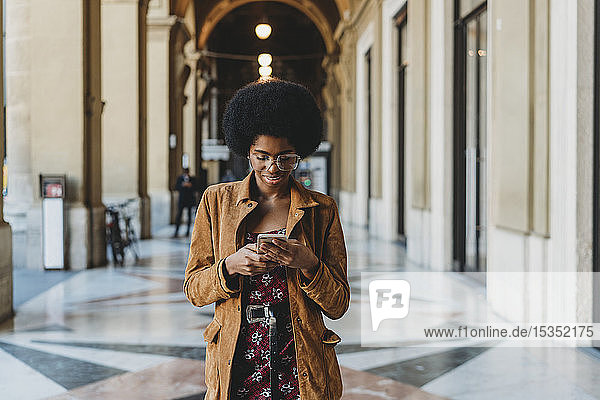 Young woman with afro hair using smartphone in building corridor
