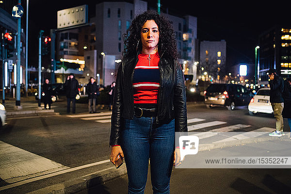 Mid adult woman with long curly hair on city street at night  portrait