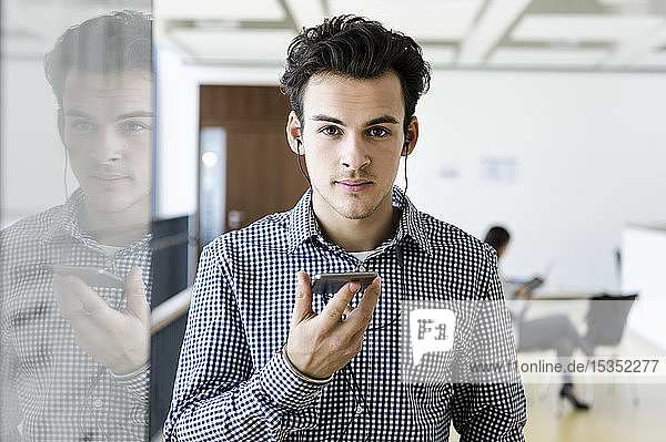 Geschäftsmann mit Smartphone im Bürokorridor  Kollege liest im Hintergrund