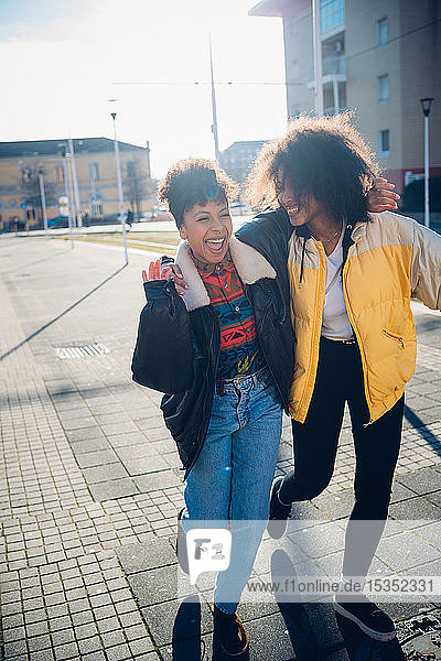 Zwei coole junge Freundinnen lachen auf dem städtischen Bürgersteig