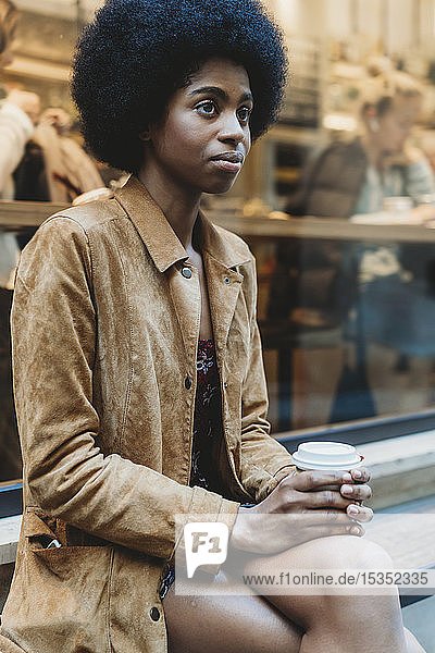 Junge Frau mit Afro-Haaren bei einem Heißgetränk vor einem Café