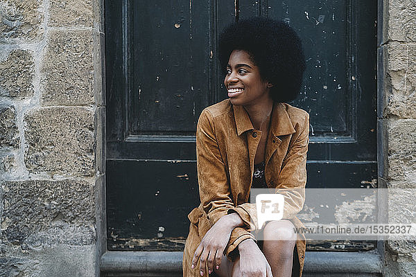 Junge Frau mit Afro-Haaren wartet an der Tür eines Steinhauses