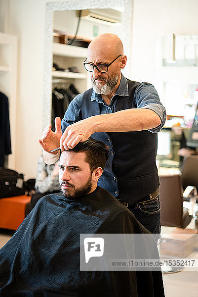 Hairdresser combing customer's hair in barber shop