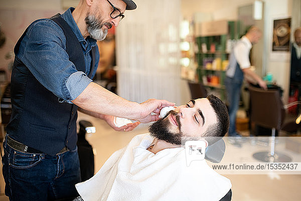 Hairdresser preparing to shave customer's beard in barber shop