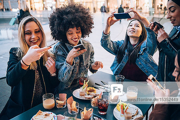 Friends taking photos of their food and drinks at outdoor cafe  Milan  Italy