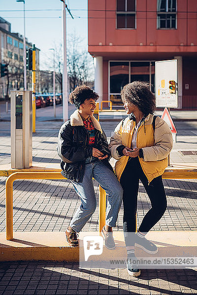 Zwei coole junge Frauen unterhalten sich an der städtischen Straßenbahnhaltestelle