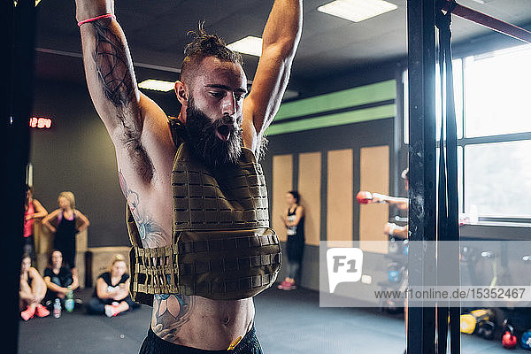 Young tattooed man training in gym  hanging from exercise bar
