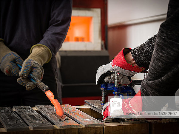 Messerfabrikarbeiter mit Zange  um rotglühendes Metall in der Werkstatt aus der Form zu entfernen  Nahaufnahme der Hände