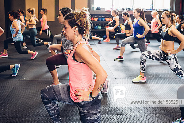 Gruppe von Frauen  die im Fitnessstudio trainieren  mit ausgestreckten Händen auf den Hüften und gestreckten Beinen
