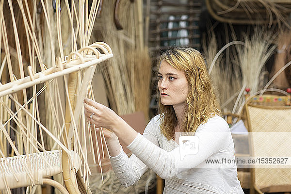 Young female basket maker weaving in workshop