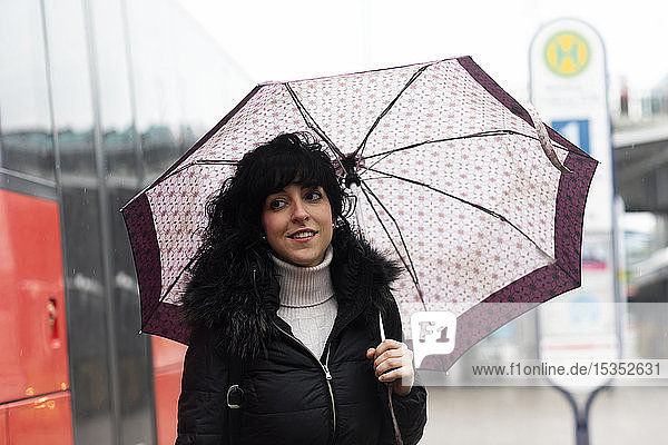 Mittlere erwachsene Frau mit Regenschirm an der städtischen Straßenbahnhaltestelle