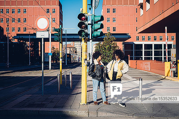 Zwei coole junge Freundinnen unterhalten sich am Fußgängerüberweg
