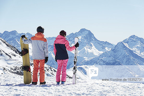 Teenager-Junge Snowboarder mit Schwester  die vom schneebedeckten Berggipfel aus den Blick auf sich zieht  Rückansicht  Alpe-d'Huez  Rhône-Alpes  Frankreich