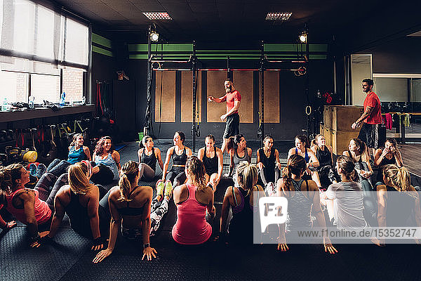 Large group of women training in gym with male trainers  sitting on floor