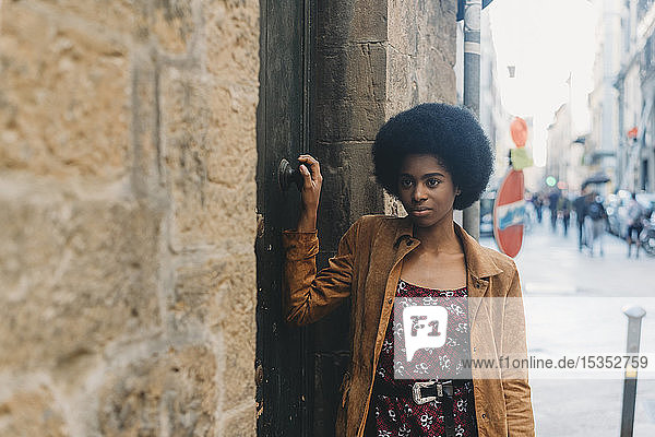 Young woman with afro hair waiting at door of stone building