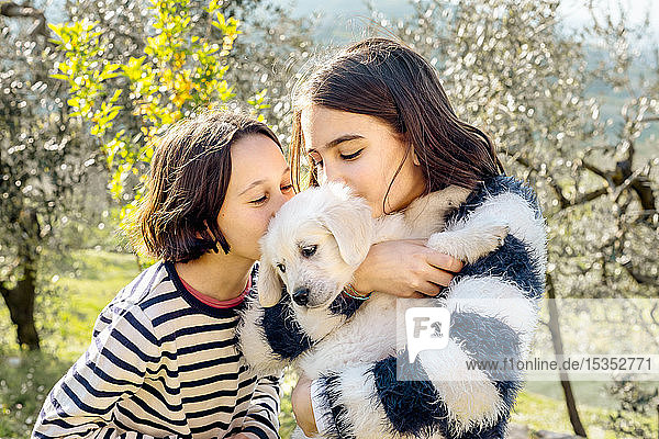Zwei Mädchen küssen einen süßen Golden Retriever-Welpen im Obstgarten  Scandicci  Toskana  Italien