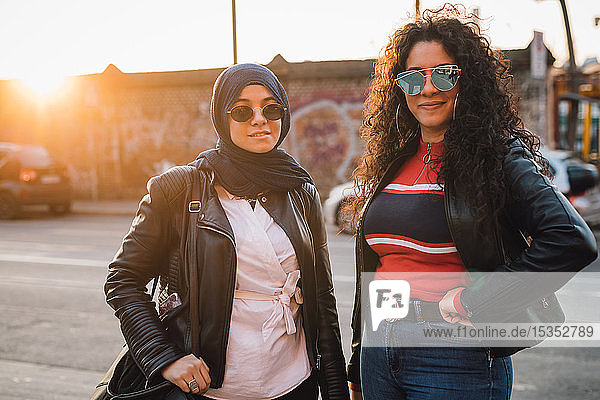 Junge Frau im Hidschab und beste Freundin in der Stadt bei Sonnenuntergang  Porträt