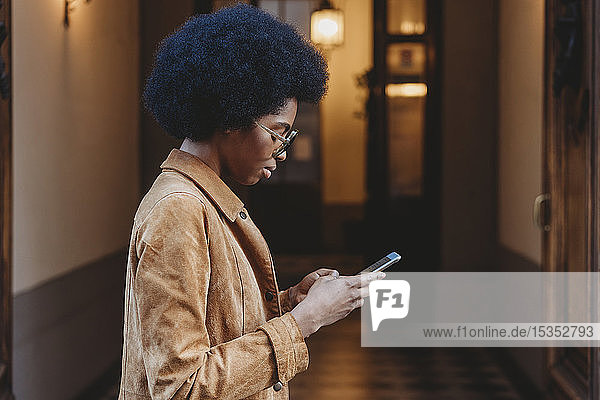 Junge Frau mit Afro-Haaren benutzt Smartphone vor dem Gebäude