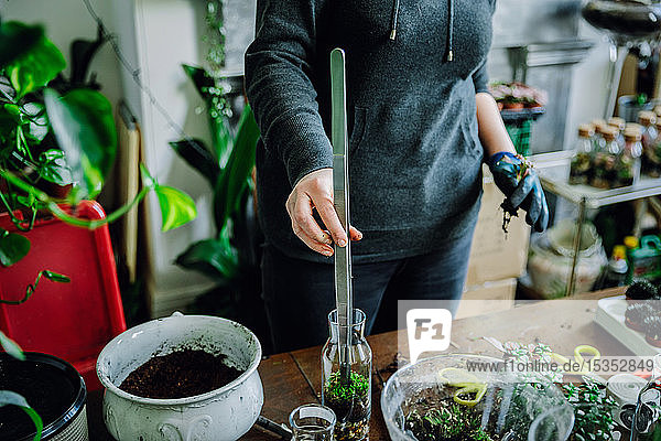 Frau füllt Glasflasche mit Pflanzen in Gärtnerei