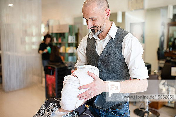 Friseur trocknet Gesicht und Haare des Kunden mit Handtuch beim Friseur