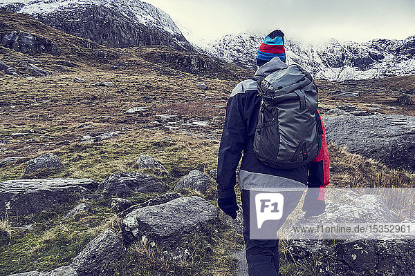 Male hiker hiking up rugged landscape with snow capped mountains  rear view  Llanberis  Gwynedd  Wales