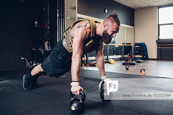 Young tattooed man training in gym  doing push ups on kettle bells