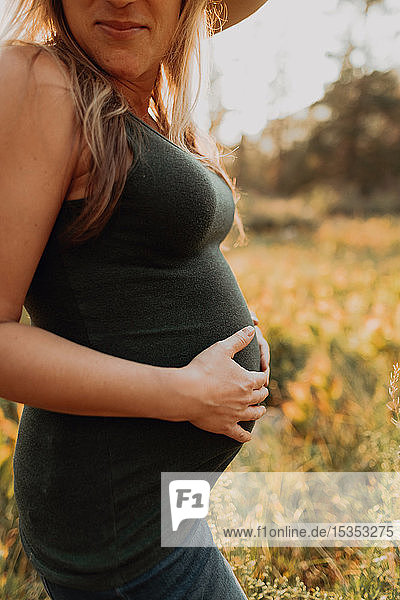 Mittelprachige schwangere Frau in Stetson mit Händen auf dem Bauch im ländlichen Tal bei Sonnenuntergang  abgeschnitten  Mineral King  Kalifornien  USA