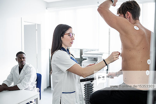 Arzt beobachtet Krankenschwester bei EKG-Test des Patienten im Sprechzimmer