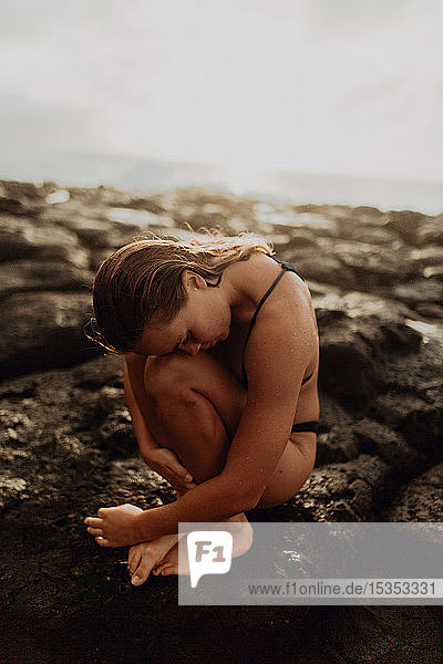 Frau sitzt zusammengerollt auf Felsen am Meer  Princeville  Hawaii  USA