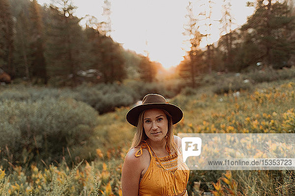 Mittelgroße erwachsene Frau mit Filzhut zwischen Wildblumen bei Sonnenuntergang im ländlichen Tal  Porträt  Mineral King  Kalifornien  USA