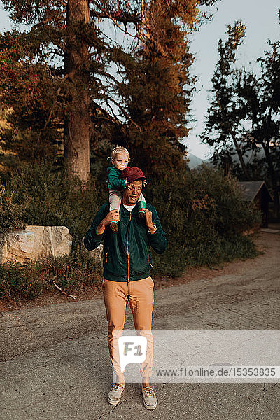 Young man carrying female toddler on shoulders on rural valley road  portrait  Mineral King  California  USA