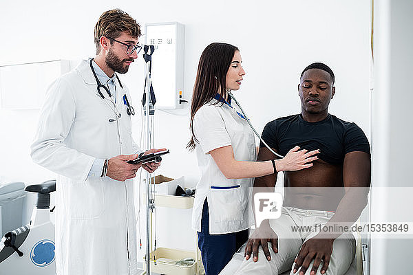 Doctor watching nurse examine patient in consultation room