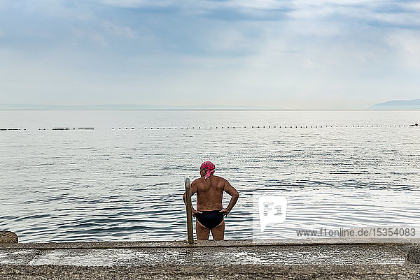 Male swimmer stands looking out at the coastline and the Adriatic Sea; Opatija  Primorje-Gorski Kotar County  Croatia