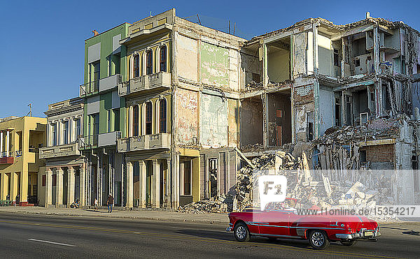 Ein altes Auto fährt an der abgerissenen Fassade eines alten Gebäudes entlang einer Straße vorbei; Havanna  Kuba