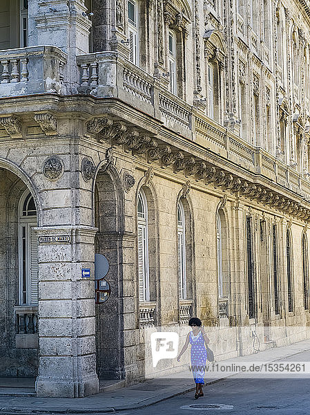A woman walks on the street beside a building with ornate facade; Havana  Cuba