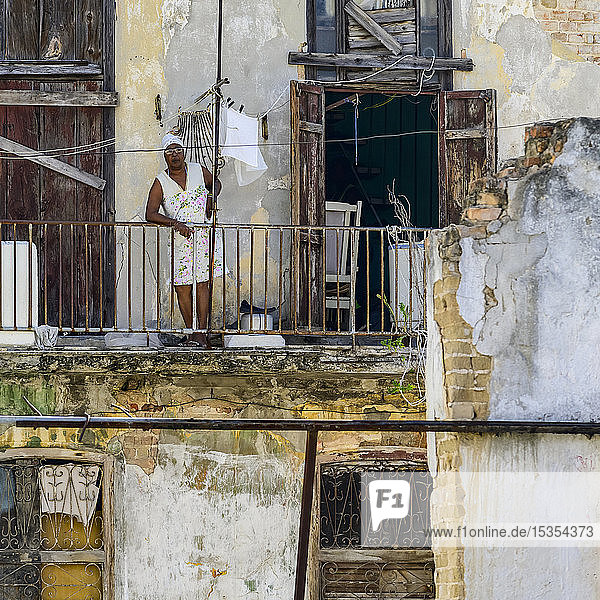Frau lehnt am Geländer ihres Balkons und blickt auf die Straßen unter ihr; Havanna  Kuba