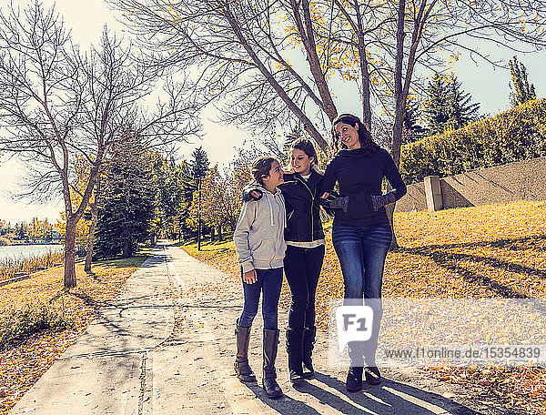 Eine Mutter und ihre beiden Töchter  die an einem warmen Herbsttag auf einem Weg in einem Stadtpark spazieren gehen und sich unterhalten; Edmonton  Alberta  Kanada