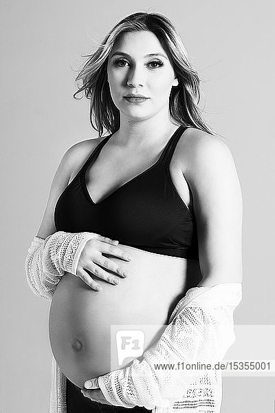 Ein Schwarz-Weiß-Foto einer jungen schwangeren Frau  die in einem Studio ihren Bauch hält und für die Kamera posiert; Edmonton  Alberta  Kanada
