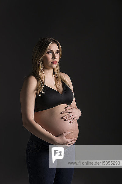 Eine junge schwangere Frau  die in einem Studio ihren Bauch hält und von der Kamera wegschaut  denkt an ihr ungeborenes Kind: Edmonton  Alberta  Kanada