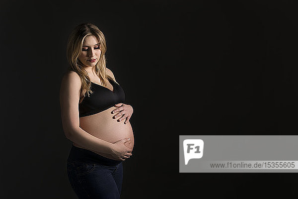 A young pregnant woman holding her belly in a studio and looking down at her unborn child; Edmonton  Alberta  Canada