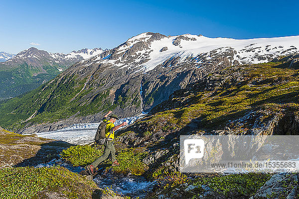 A man backpacking near a small stream in Kenai Fjords National Park with Exit Glacier in the background on a sunny summer day in South-central Alaska; Alaska  United States of America
